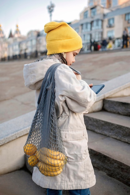 通りの階段に座って、買い物からの途中でスマートフォンでテキストメッセージを送るプレティーンの女の子