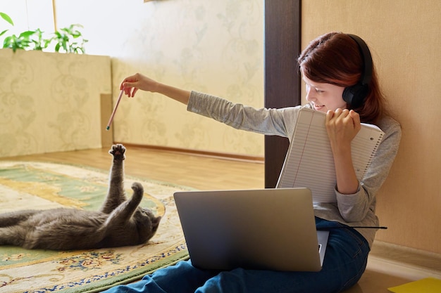 Preteen girl studying at home using laptop along with cat