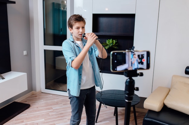 Preteen at home sing to microphone. Young American boy working as web influencer,