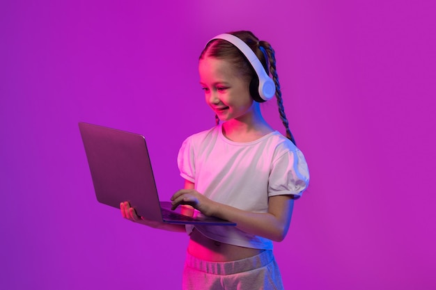 Preteen kid adorable girl using wireless headphones and laptop