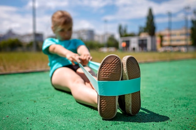 Foto preteen meisje maakt oefeningen met fitness weerstandsband op openbare sportveld in stadssport