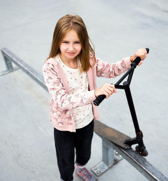 Preteen meisje staat met scooter op straat in het park en kijkt naar camera schattig kind poserend verstand