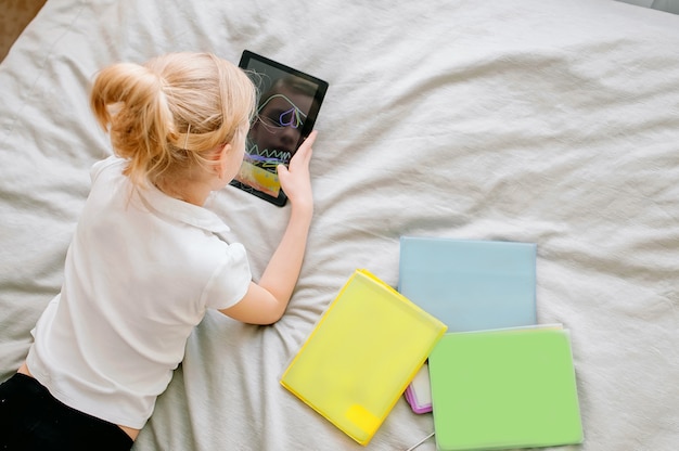 Preteen schoolgirl doing her homework with digital tablet at home. Child using gadgets to study. Education and distance learning for kids. Homeschooling during quarantine. Stay at home entertainment.