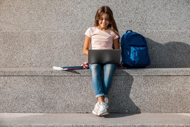 Preteen schoolgirl sitting on the stairs outside and using laptop