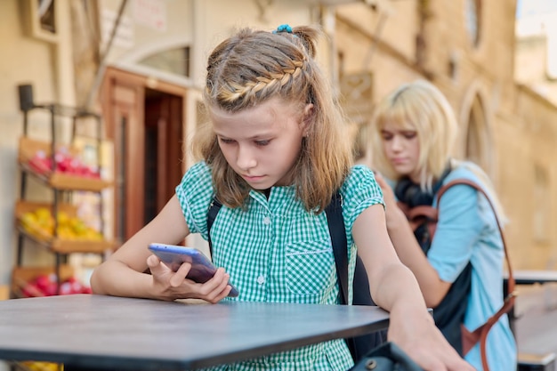 Preteen schoolmeisje en tiener student met rugzakken met smartphones buiten