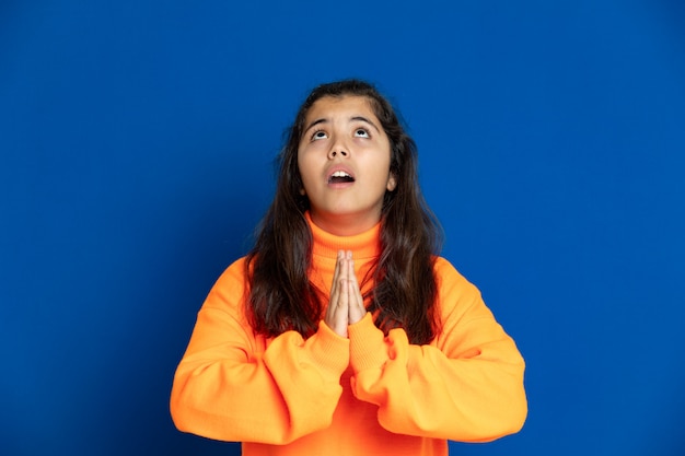 Preteenmeisje met het gele gesturing van jersey over blauwe muur