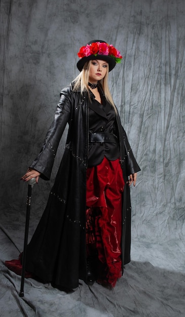 A pretentious gothic lady in a long leather coat and a hat with roses uses a cane