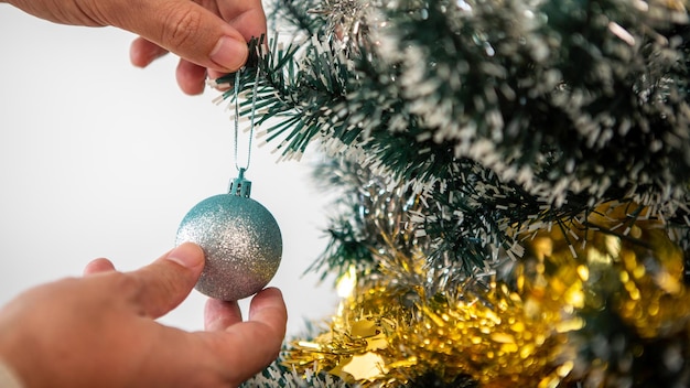 Prettige kerstdagen en fijne feestdagen, de hand van een man versiert de spar binnenshuis in de winter. xmas ballen en klatergoud opknoping van dennentakken voor decoratie banner, nieuwjaar concept.