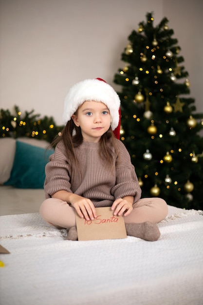 Prettige kerstdagen en fijne feestdagen Het kleine gelukkige meisje op het bed schreef een brief aan de kerstman en houdt de envelop in haar hand