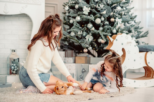 Prettige kerstdagen en fijne feestdagen. moeder en dochter aaien een hond in de buurt van de kerstboom binnenshuis. liefdevolle familie in de kamer