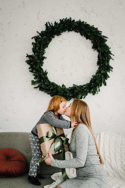 Prettige kerstdagen en fijne feestdagen Moeder geeft een geschenk aan haar dochter bij de kerstboom Vrolijke moeder knuffelt schattige baby meisje samen thuis Gelukkig Nieuwjaar 2021