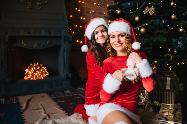 Prettige kerstdagen en fijne feestdagen! mooie moeder met dochtertje in kerstkostuums brengen samen tijd door in de buurt van de kerstboom.