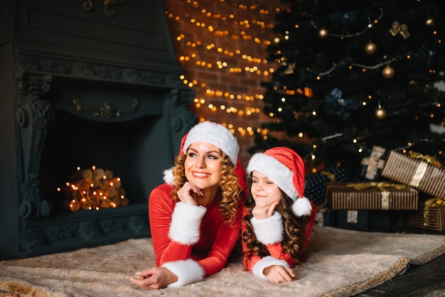 Prettige kerstdagen en fijne feestdagen! Mooie moeder met dochtertje in kerstkostuums brengen samen tijd door in de buurt van de kerstboom.