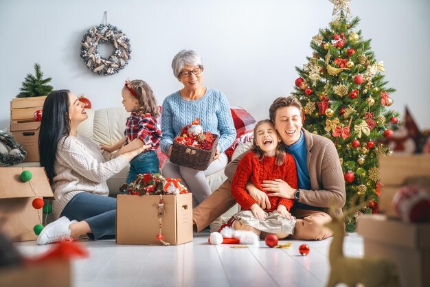 Prettige kerstdagen en fijne feestdagen! Oma, moeder, vader en kinderen versieren de boom in de kamer. Liefdevolle familie binnenshuis.