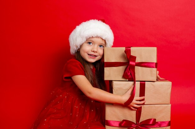 Prettige kerstdagen en fijne feestdagen Portret van emotioneel meisje in een kerstmuts op een rode achtergrond