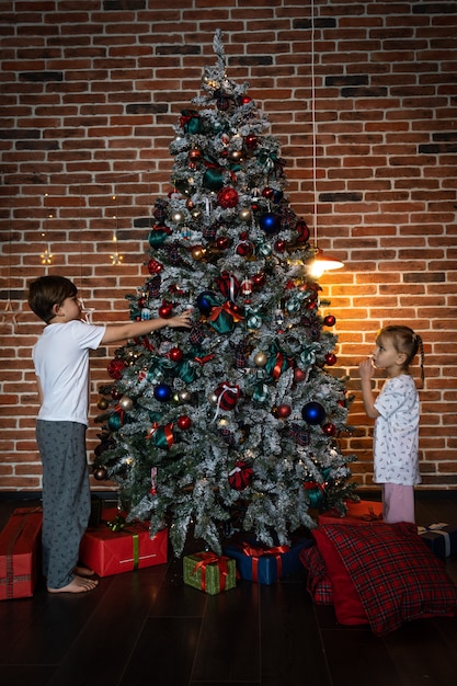 Prettige kerstdagen en fijne feestdagen. Schattig klein kind meisje en jongen versieren de kerstboom binnenshuis.