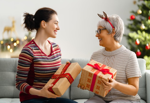 Prettige kerstdagen en fijne feestdagen! Senior moeder en haar volwassen dochter wisselen geschenken uit. Plezier in de buurt van de boom binnenshuis. Liefdevolle familie met cadeautjes op de kamer.