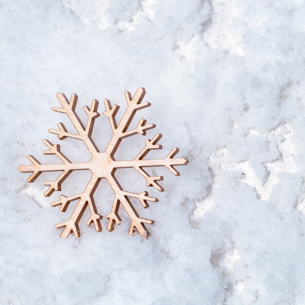 Prettige kerstdagen en gelukkig Nieuwjaar wenskaart met houten sneeuwvlok op sneeuw achtergrond met kopie ruimte. Plat leggen. Bovenaanzicht.