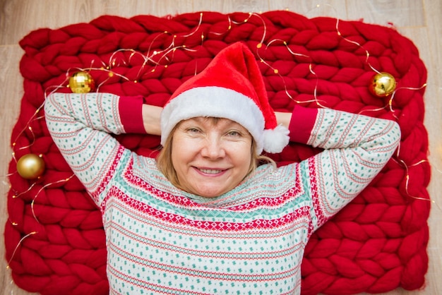 Prettige kerstdagen, fijne feestdagen en nieuwjaar. Senior in kerstmuts ligt op zachte rode gebreide merino wollen deken