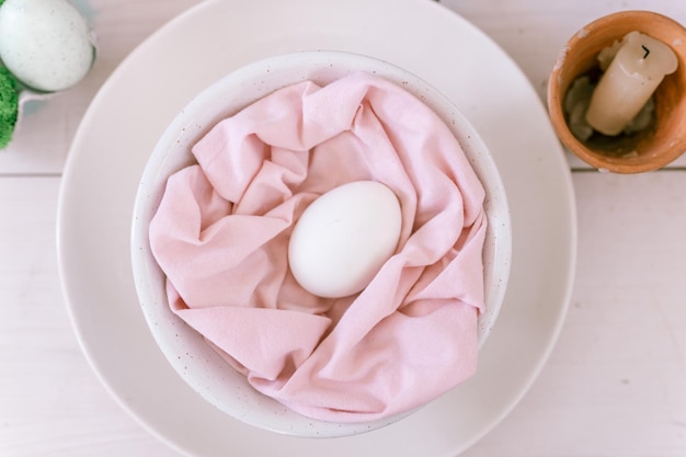 Foto prettige paasvakantie in het lenteseizoen feestelijk huisdecor traditioneel eten natuurlijk wit kippenei in pastelroze stof in een bord op tafel