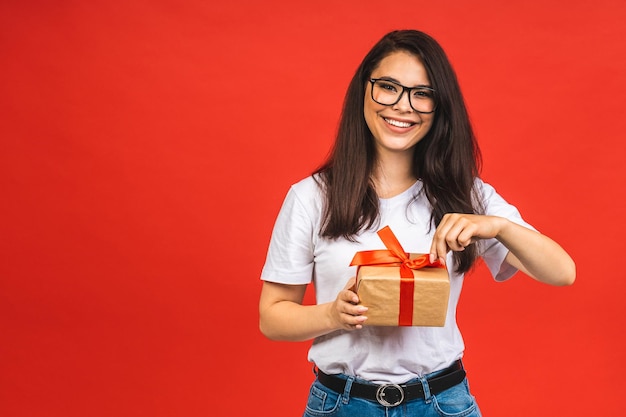 Prettige vakantie Studio portret van lachende jonge mooie brunette vrouw houdt geschenkdoos geïsoleerd op rode achtergrond