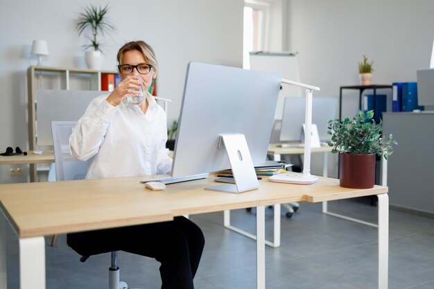 Pretty adult business woman in the office drinking water while working at a computer