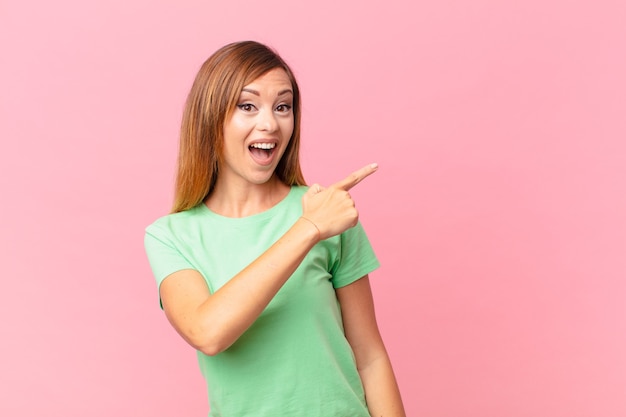 Pretty adult woman looking excited and surprised pointing to the side