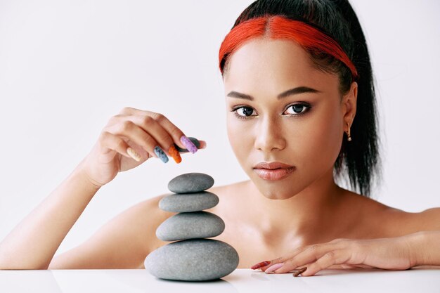 Pretty african american woman doing pyramid of the stones on\
white background