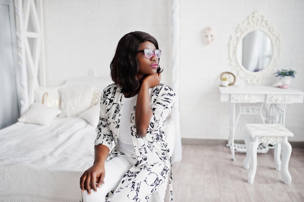 Pretty african american woman in eyeglasses black and white dress posed in room