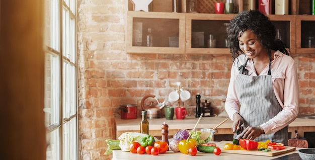 pretty african american woman preparing healthy veggies salad at kitchen and smiling copy space