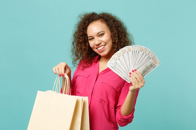 Pretty african girl hold package bag with purchases after shopping, fan of money in dollar banknotes, cash money isolated on blue turquoise background. People lifestyle concept. Mock up copy space.