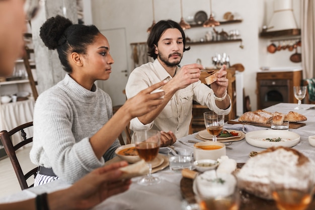 写真 かなりアフロアメリカ人の女性と髭を生やしたハンサムな男が夢のようにパンを食べてテーブルに座っています