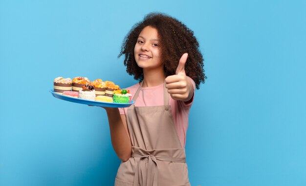 Pretty afro teenager feeling proud, carefree, confident and happy, smiling positively with thumbs up. humorous baker concept