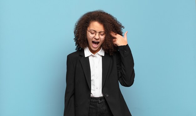 Pretty afro teenager looking unhappy and stressed, suicide gesture making gun sign with hand, pointing to head. humorous business concept