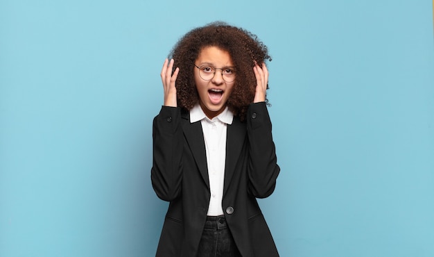 Pretty afro teenager screaming with hands up in the air, feeling furious, frustrated, stressed and upset. humorous business concept