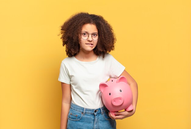 Adolescente abbastanza afro che sorride allegramente, si sente felice e punta di lato e verso l'alto, mostrando l'oggetto nello spazio della copia. concetto di risparmio