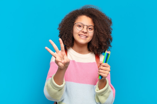 Pretty afro teenager smiling and looking friendly, showing number three or third with hand forward, counting down. student concept