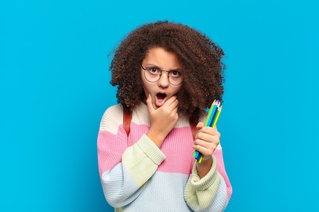 Pretty afro teenager with mouth and eyes wide open and hand on chin