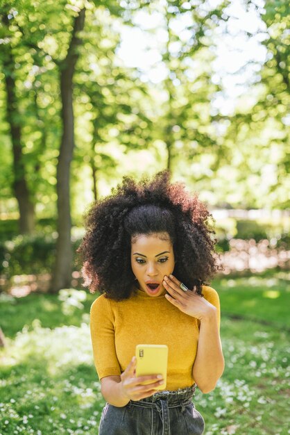 Pretty afro woman chatting surprised, in a park. Selective focus.