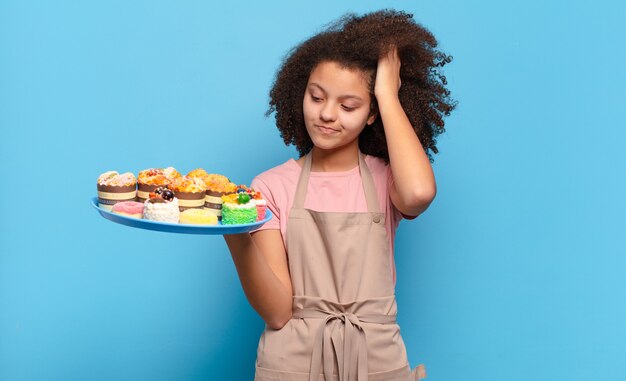 Pretty afro woman feeling puzzled and confused, scratching head and looking to the side. humorous baker concept