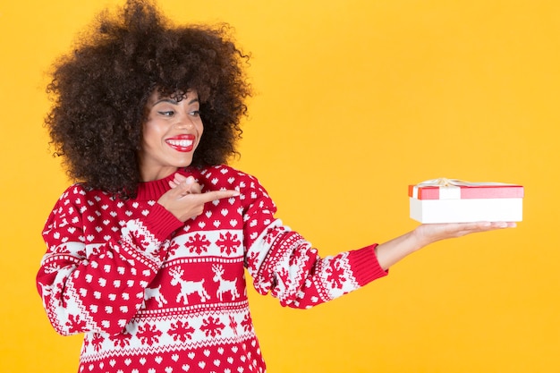 Pretty afro woman with christmas clothes and a gift in her hands, yellow background
