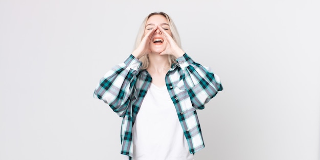 pretty albino woman feeling happy, excited and positive, giving a big shout out with hands next to mouth, calling out