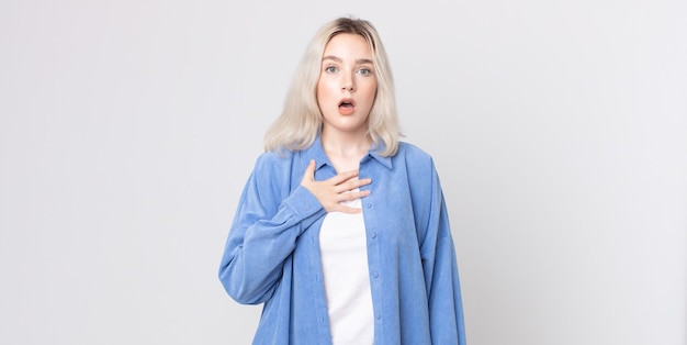 Pretty albino woman feeling shocked, astonished and surprised, with hand on chest and open mouth, saying who, me?