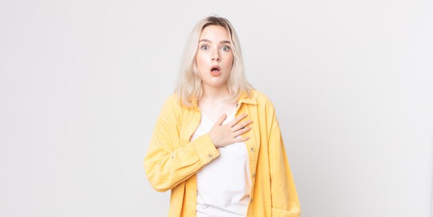 Pretty albino woman feeling shocked and surprised, smiling, taking hand to heart, happy to be the one or showing gratitude