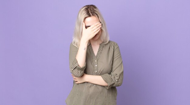 pretty albino woman looking stressed, ashamed or upset, with a headache, covering face with hand