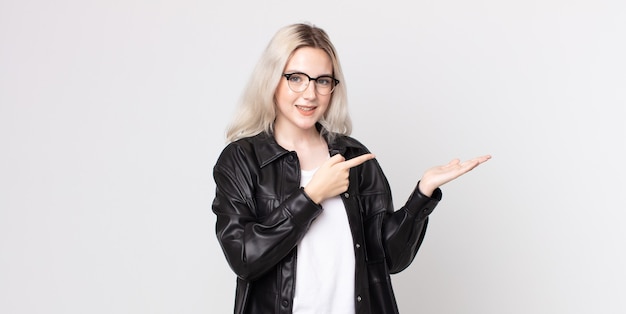 Pretty albino woman smiling cheerfully and pointing to copy space on palm on the side, showing or advertising an object