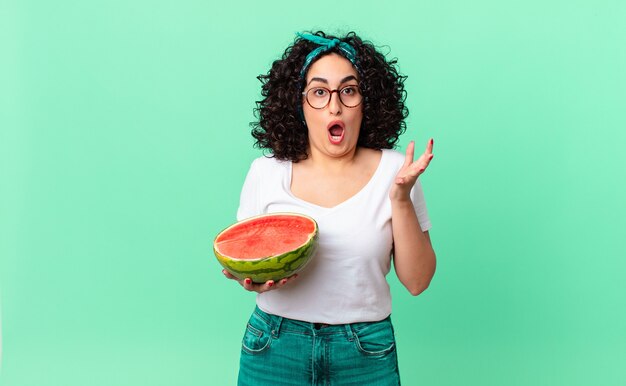 Pretty arab woman amazed, shocked and astonished with an unbelievable surprise and holding a watermelon. summer concept