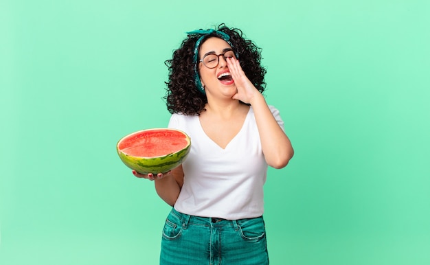 Pretty arab woman feeling happy,giving a big shout out with hands next to mouth and holding a watermelon. summer concept