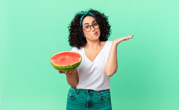 かなりアラブの女性は、戸惑い、混乱し、スイカを疑って抱きしめていると感じています。夏のコンセプト