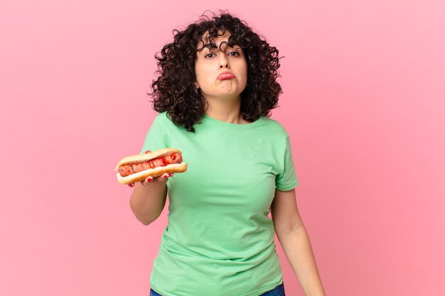 pretty arab woman feeling sad and whiney with an unhappy look and crying and holding a hot dog